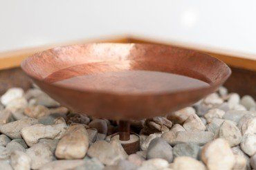 Kupferne Schale mit Wasser auf Steinen.