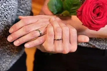 Zwei Hände mit Eheringen, eine rote Rose.